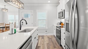 A modern kitchen with white cabinetry, stainless steel appliances, and a wooden floor. - Laguna Haven! 3BR 2BA Sleeps 7! Your Perfect Escape! (Panama City Beach)