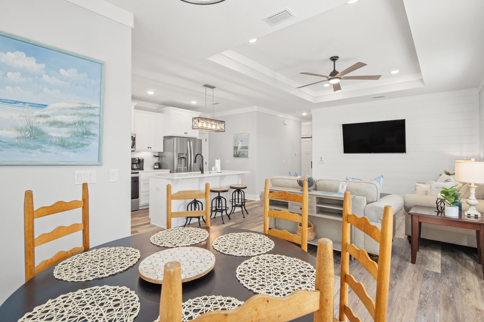 A modern kitchen with white cabinets, a stainless steel refrigerator, and a dining area with wooden chairs and a table with placemats.