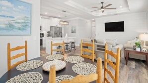 A modern kitchen with white cabinets, a stainless steel refrigerator, and a dining area with wooden chairs and a table with placemats. - Laguna Haven! 3BR 2BA Sleeps 7! Your Perfect Escape! (Panama City Beach)