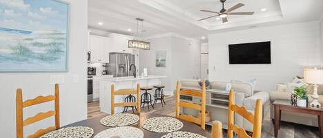 A modern kitchen with white cabinets, a stainless steel refrigerator, and a dining area with wooden chairs and a table with placemats.