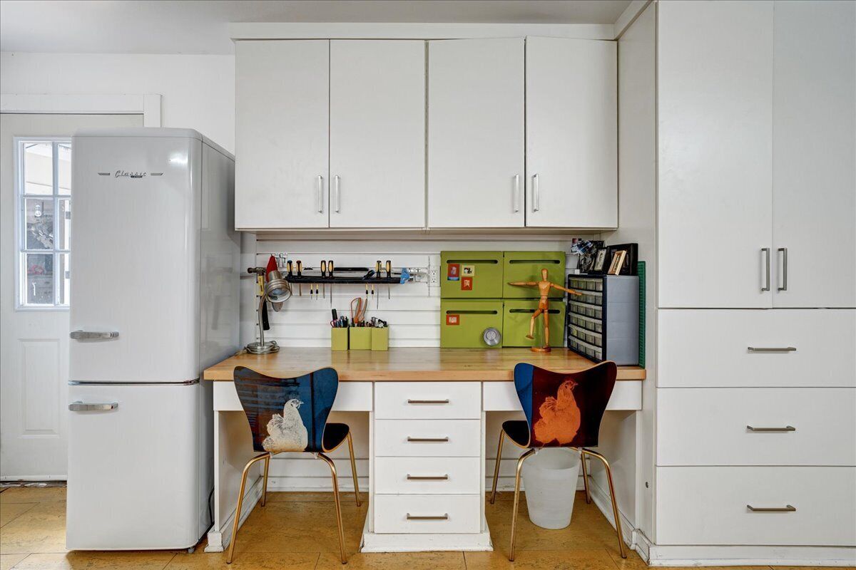 A compact kitchen with white cabinets, a white refrigerator, and two chairs with colorful upholstery.