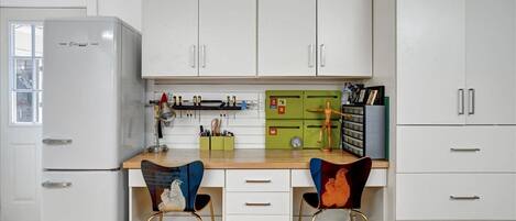 A compact kitchen with white cabinets, a white refrigerator, and two chairs with colorful upholstery.