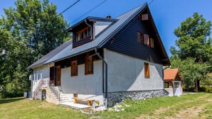 Una casa de madera de dos pisos con techo inclinado, cimientos de piedra y un pequeño porche con un banco.