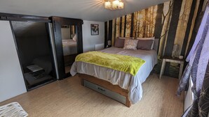 A bedroom with a bed, a bedside table, a mirror, a wardrobe, and a wall with a forest-themed wallpaper. - Cozy cabin loft with a giant soaking tub just 30 minutes from Yellowstone (Island Park)