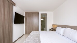 A hotel room with a bed, a TV mounted on the wall, a bedside table with a lamp, and a wooden wardrobe. - Urban studio in Laureles with nice view near Unicentro Mall (Medellín)
