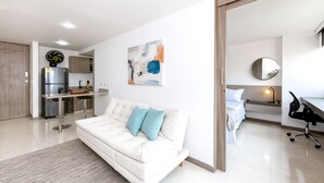 A modern living room with a white sofa, a kitchen area, and a bedroom with a bed and desk. - Urban studio in Laureles with nice view near Unicentro Mall (Medellín)
