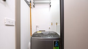 A compact, stainless steel washer-dryer unit in a narrow hallway with white walls, a visible electrical outlet, and a small sign indicating a 5-year warranty. - Urban studio in Laureles with nice view near Unicentro Mall (Medellín)