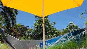 A pool area with a yellow umbrella, a bottle, and a laptop on the ground. - Private Studio, with to much space at the gardens and many amenities like pool. (Toa Alta)