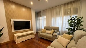 A living room with a flat-screen TV, a beige sofa, a small armchair, and a wooden accent wall.