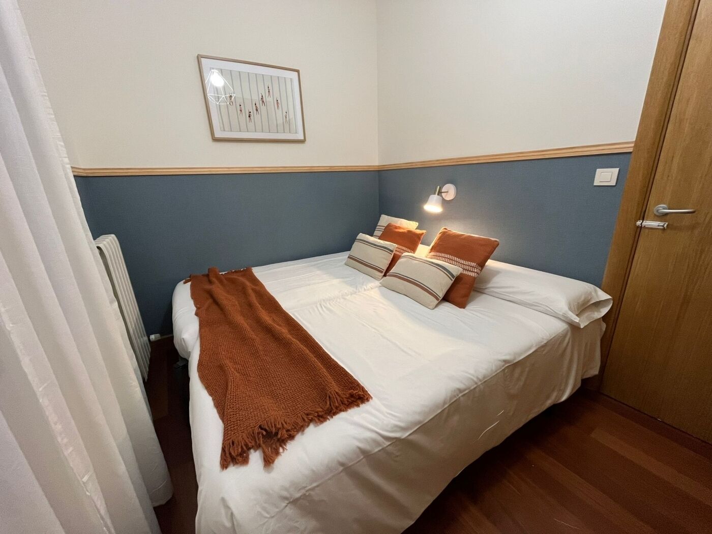 Un lit bien fait, avec un plaid marron et des oreillers, un tableau encadré accroché au mur et une lampe de chevet.