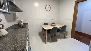 A compact kitchen with a dining table and chairs, a kettle, and a clock on the wall.