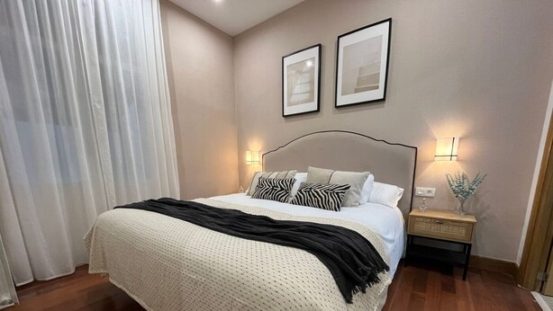 A neatly made bed with a white duvet and black throw, a bedside table with a lamp, and a wall-mounted picture frame.