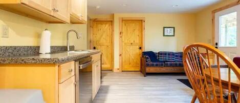 A kitchen with wooden cabinets, a granite countertop, and a sink. There is a wooden dining table with chairs and a bench with a plaid blanket.