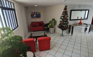Un salon avec un canapé rouge, une table basse en verre, une plante en pot, un sapin de Noël et un tableau encadré accroché au mur.