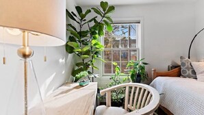Tunnelmallinen makuuhuone, jossa on sänky, tuoli, lamppu ja useita ruukkukasveja.