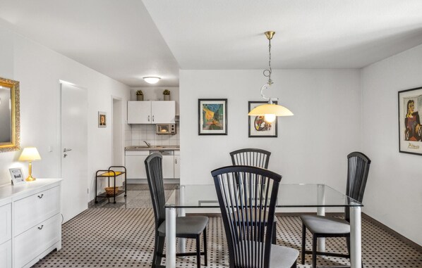 Una cocina moderna con armarios blancos, microondas y comedor con mesa de vidrio y sillas negras.