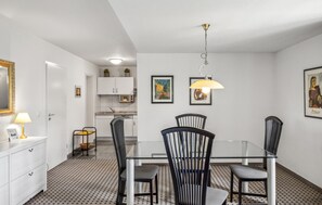 Une cuisine moderne avec des meubles blancs, un four à micro-ondes et un coin repas comprenant une table en verre et des chaises noires.