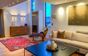 Een moderne woonkamer met een bank, een salontafel, een open haard en uitzicht op de stad door een groot raam.