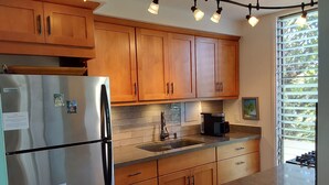A kitchen with wooden cabinets, a stainless steel refrigerator, a coffee maker, and a window with blinds.