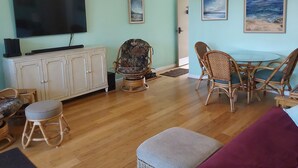 A living room with a television, wicker furniture, a ceiling fan, and artwork on the walls.