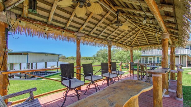 Une terrasse extérieure avec des chaises en osier et une table en bois, donnant sur une pelouse et un bâtiment.