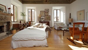 Una habitación amplia con una cama grande, una chimenea, una mesa de madera y una silla.