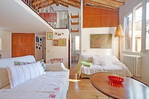 Une chambre avec deux lits, une table en bois, un escalier et une vue sur l’extérieur.