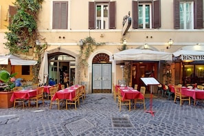 Un café en plein air avec des tables et des chaises, une rue pavée et un bâtiment doté d’une porte et de fenêtres.