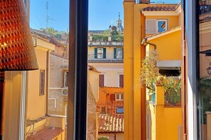 Une rue étroite bordée d’immeubles, une fenêtre avec un rideau et une plante sur le balcon.
