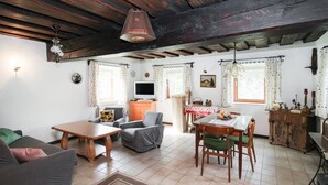 A cozy living room with a sofa, a dining table with chairs, a TV, and a kitchen area with a window. - Ferienhaus in Idylle St. Peter (Aspangberg - St.Peter)