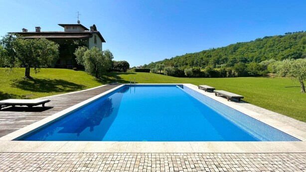 A rectangular swimming pool with a wooden deck and lounge chairs, surrounded by a well-maintained lawn and a house in the background.