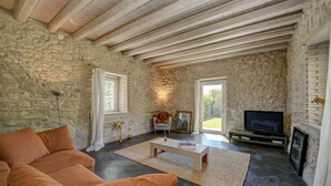 A living room with stone walls, a wooden ceiling, a sofa, a coffee table, a television, and a fireplace.
