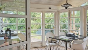 A covered patio with a glass table and white chairs, overlooking a garden.