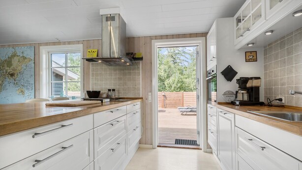 A modern kitchen with white cabinets, a stainless steel range hood, and a large window.