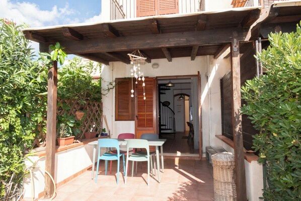 A covered patio with a table and chairs, wooden shutters, and potted plants.