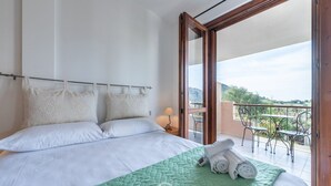 Et hotelværelse med en seng, et grønt quilt og en balkon med udendørs møbler.