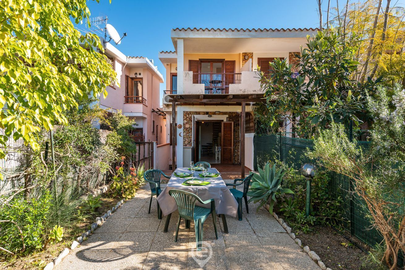 Une terrasse avec une table dressée pour le repas, entourée de verdure et avec une maison en arrière-plan.