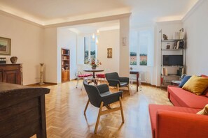 Un salón espacioso con suelo de madera, un sofá rojo, dos sillones negros, una mesa de comedor con sillas y una estantería.