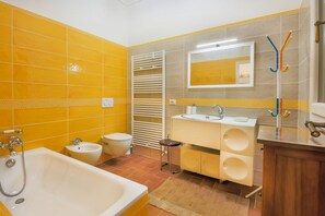 Un baño con baldosas amarillas, una bañera, un lavabo, un espejo y un perchero para toallas.