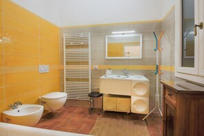 Et badeværelse med gule flisevægge, en hvid vask, et toilet og en bidét.