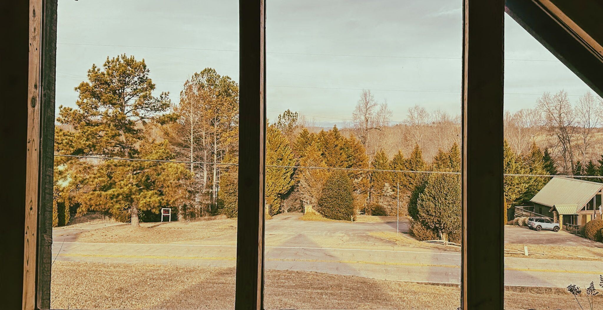 Vue depuis l’intérieur d’un bâtiment, donnant sur un parking bordé d’arbres, avec un autre bâtiment visible au loin.