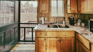 Une cuisine rustique avec des meubles en bois, un évier à deux bacs et une fenêtre équipée de stores.