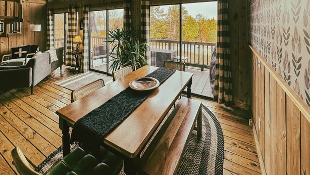 Un intérieur en bois comprenant un coin repas, de grandes fenêtres et une vue sur les arbres.