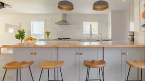 Cozinha moderna com ilha central, banquetas, iluminação pendente e vista para a sala de jantar.