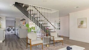 Uma sala de estar moderna com escada, dois poltronas, uma mesa de centro e um tapete.