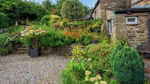 A garden with a stone wall, gravel path, and various plants. - 4 bedroom accommodation in Hawes (Hawes)
