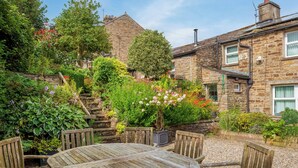 A stone building with a garden, a wooden table, and chairs. - 4 bedroom accommodation in Hawes (Hawes)