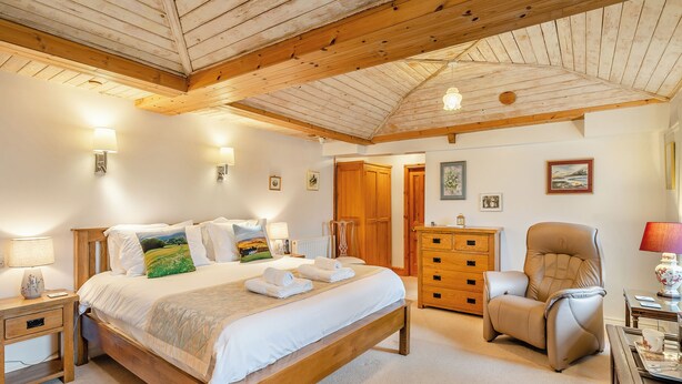 A bedroom with a wooden bed, bedside tables, a dresser, a chair, and a desk with a lamp. - 4 bedroom accommodation in Hawes (Hawes)