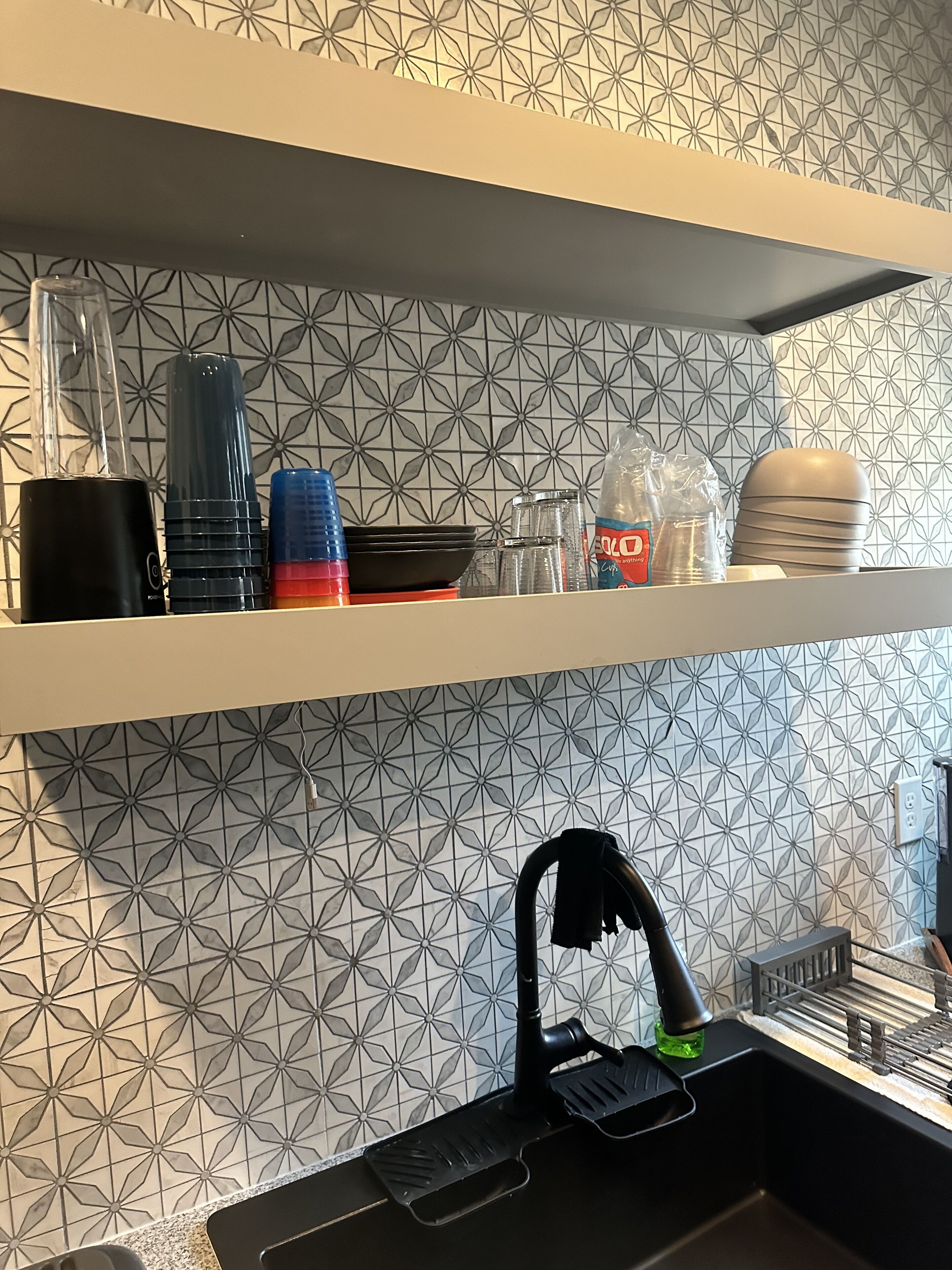 A kitchen with a patterned backsplash, a coffee machine, a kettle, and a sink with a faucet.