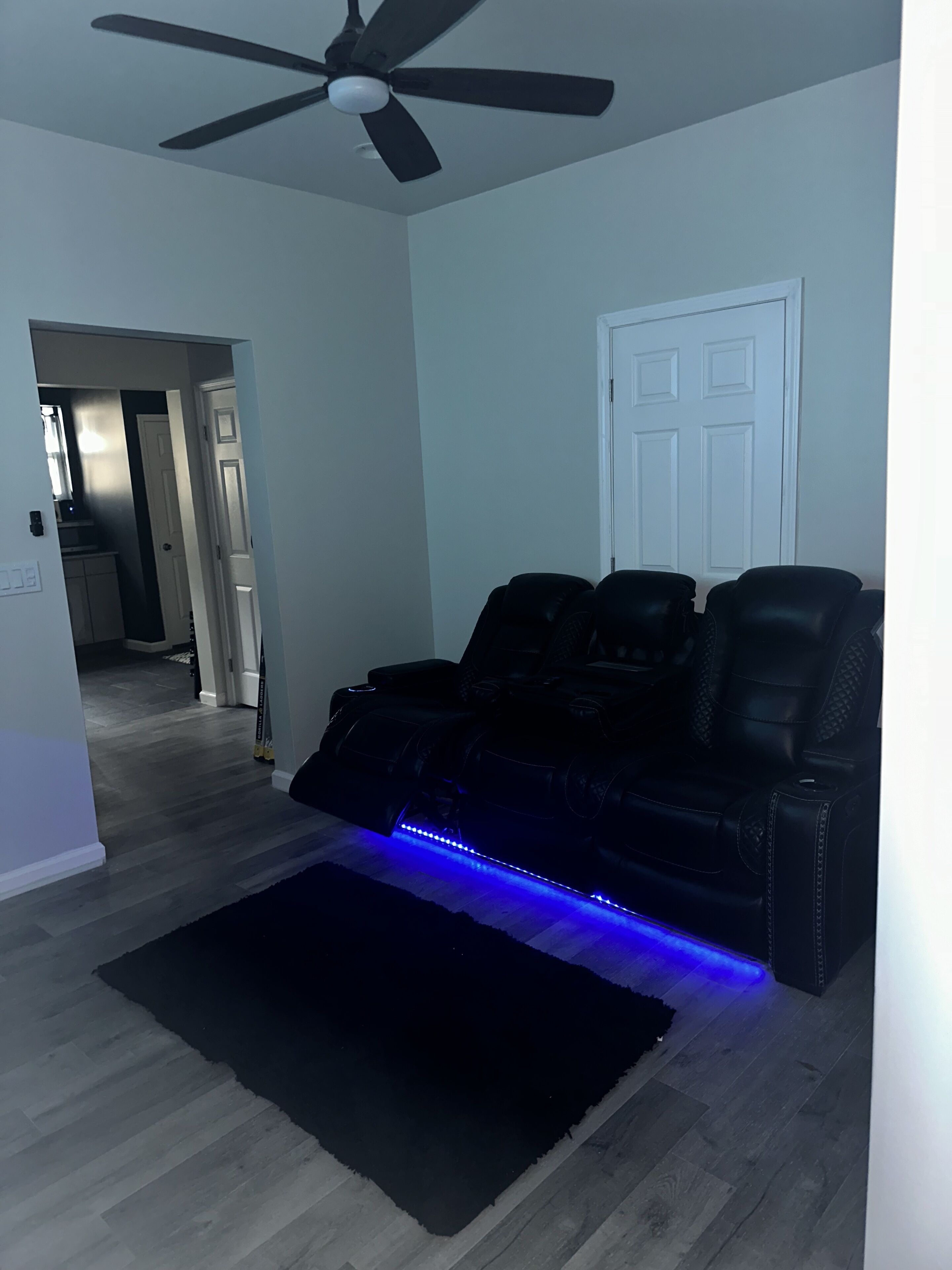 A living room with a black leather sofa, a ceiling fan, and a blue LED-lit rug.